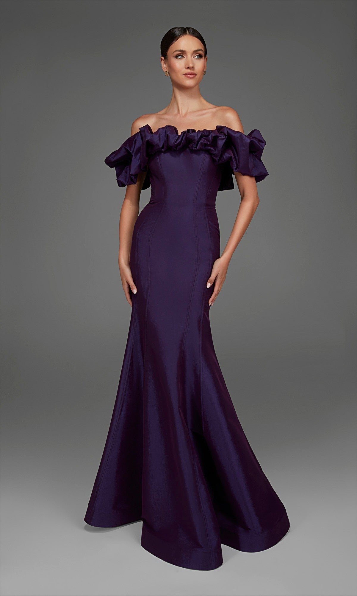A woman wearing the Alyce 27895, a floor-length, off-the-shoulder, dark purple taffeta formal dress featuring a ruffled neckline and mermaid skirt, stands against a plain gray background.